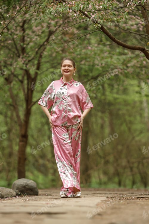 Preview: Young woman in pink national costume of Japan, walking in a garden with blooming sakura