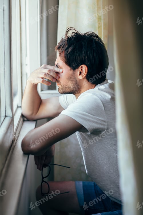 Preview: Tired young man in depression crying near window