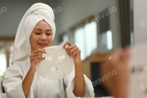 Preview: Image of youthful woman wearing bath towel on her head applying in sheet face mask.