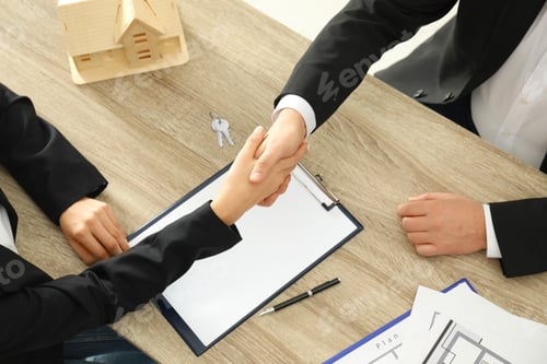 Preview: Real estate agent shaking hands with client at table in office, above view