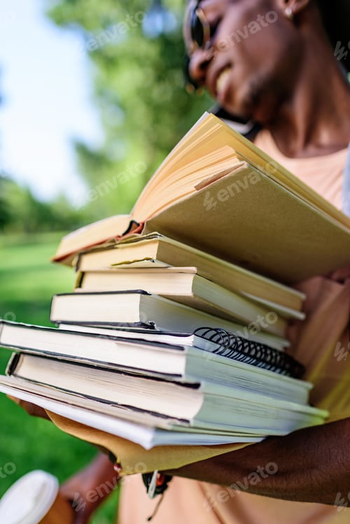 Preview: close-up view of young african american man holding pile of books in park