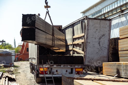 Preview: Crane Offloads Metal Bars to Truck at Construction Site