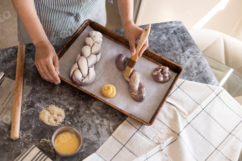 Preview: Woman makes purple challah in the kitchen, smears butter with a brush. Challah with carrot powder.