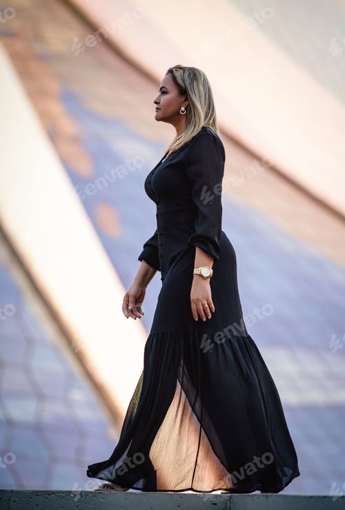 Preview: Stylish woman walking against modern architecture.