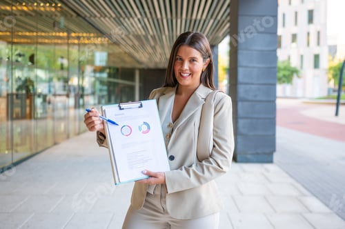 Preview: Businesswoman showing financial chart on clipboard in front of modern office building