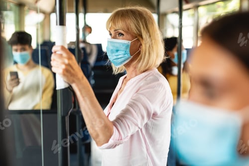 Preview: Older female in face mask standing in bus using tissue