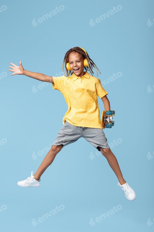 Preview: Gleeful little boy with african dreads listening music in headphones dancing over blue background.