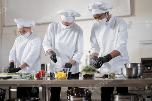 Preview: Chefs in face masks prepare takeaway food in professional kitchen