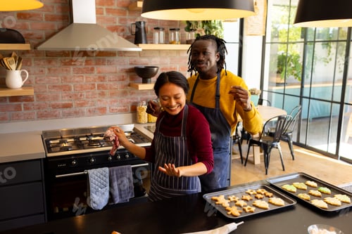 Preview: Happy diverse couple in aprons baking christmas cookies, dancing in kitchen, copy space