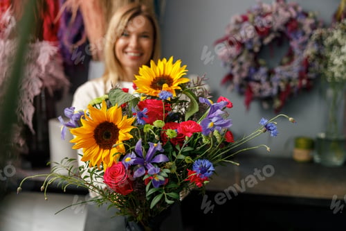 Preview: Woman flower shop owner in apron holding bouquet of flowers at florist store and looking at camera
