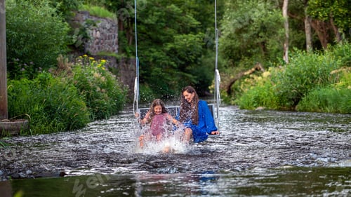 Preview: a woman and a young girl are swinging across a fast-flowing river, laughing and splashing with water