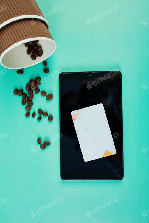 Preview: Spilled Coffee Beans Near a Takeaway Cup and Tablet With Credit Card on Teal Background