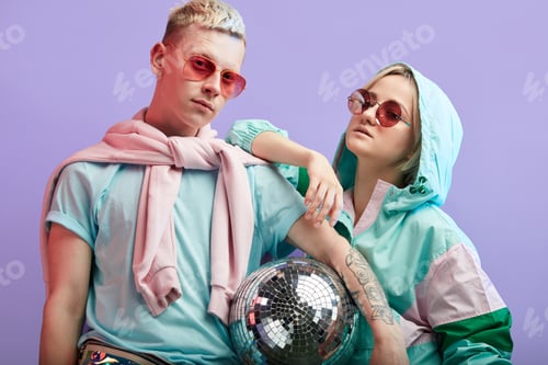 Preview: Young fashionable couple of dancers posing with disco ball on violet background