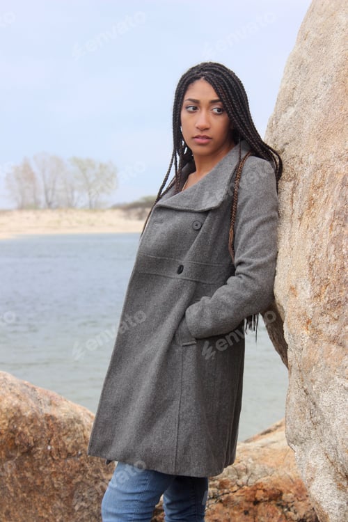 Preview: Beautiful black millennial Woman in Coat Leaning Against Rock
