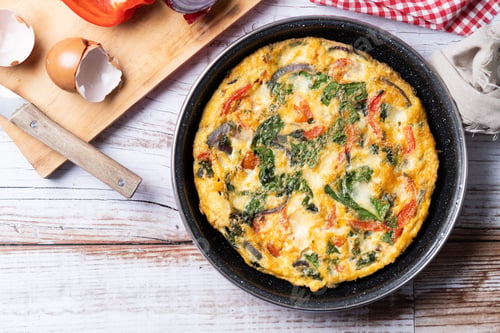 Preview: Italian Frittata made with spinach, tomatoes, onion and peppers on white wooden table