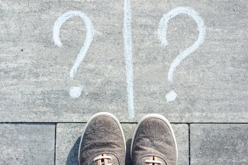 Preview: Two question marks are handwritten on an asphalt road with sneakers