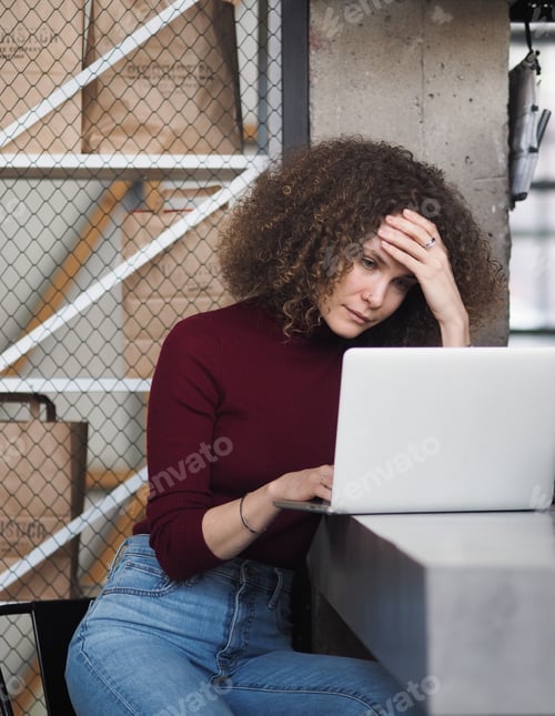 Preview: Portrait young pretty focused curly overstressed woman in causal clothes with laptop in modern cafe.