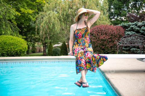 Preview: Woman in a dress sitting on a diving board above an inground swimming pool