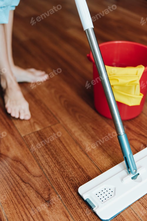 Preview: Woman cleaning wooden floor with mop and bucket of cleaning solution, water bucket nearby