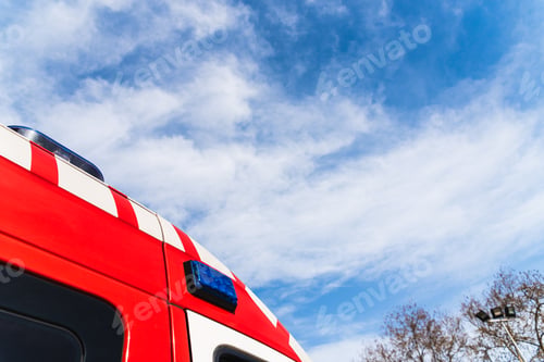 Preview: Red roof of a medicalized ambulance over blue sky with clouds and copy space