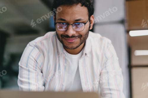 Preview: Happy bearded man in eyeglasses standing against blurred background in office