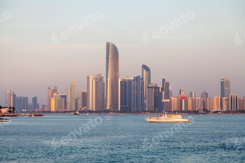 Preview: Abu Dhabi cityscape at the golden hour. View from the seaside with white boat at the foreground.