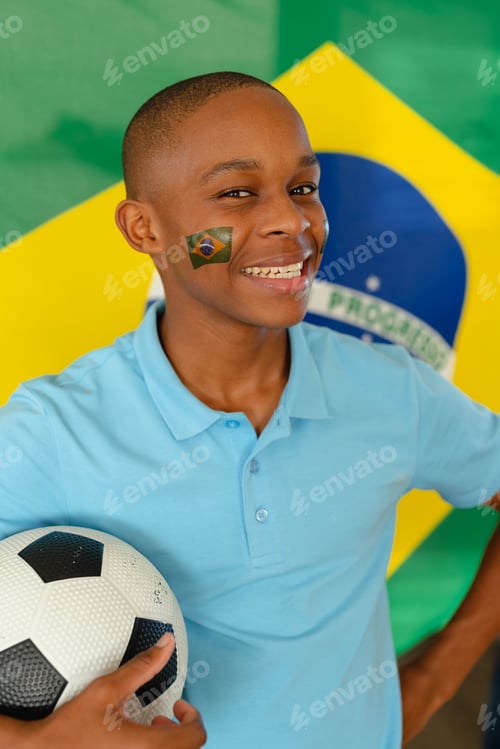 Preview: Portrait of happy african american male teenager with flag of brazil and football