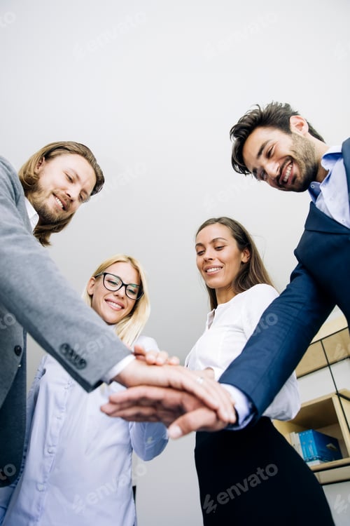Preview: Young coworkers putting hands together as symbol of unity in the office
