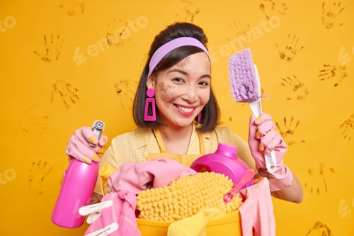 Preview: Image of positive housewife smiles pleasantly holds cleaning tools enjoys working process poses with