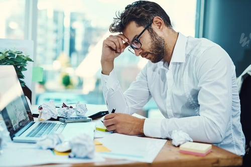 Preview: Shot of a young businessman looking stressed out while working on a laptop in an office