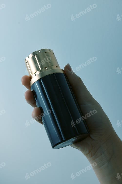 Preview: Hand holding black and gold perfume bottle on blue background with copy space in top right corner