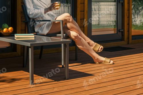 Preview: Bare legs of unrecognizable woman in a robe on a deck chair basking in the sun