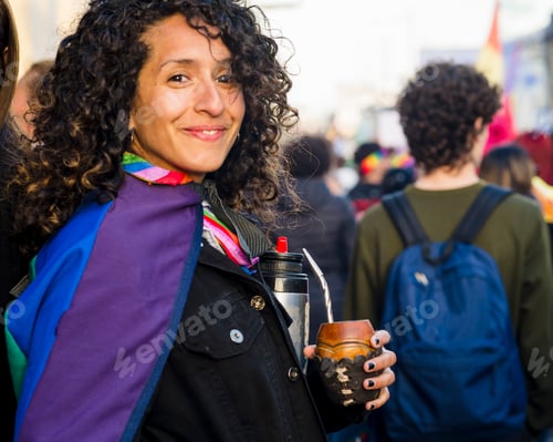 Preview: Woman looking at camera while holding a mate with a rainbow flag in an lgbtq pride march.