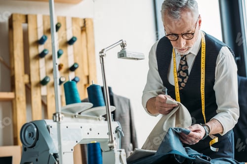 Preview: handsome tailor choosing between dark and light clothes at sewing workshop