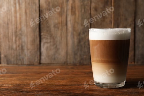 Preview: Glass of delicious layered coffee on wooden table, space for text