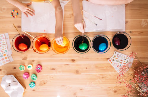 Preview: Children paint eggs for Easter in glass plates with paint on a wooden table