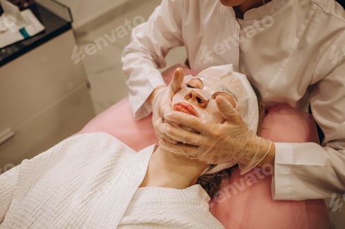 Preview: woman cosmetologist apply white clay mask on woman's face. Beautiful brunette woman in beauty salon