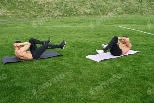 Preview: Two men doing abs crunches on grass of outdoors stadium