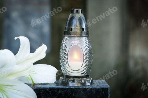 Preview: Lilies and grave lantern with burning candle on tombstone in cemetery, space for text