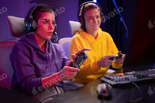 Preview: Two woman gamers wearing headsets playing a video game together in a colorful gaming room
