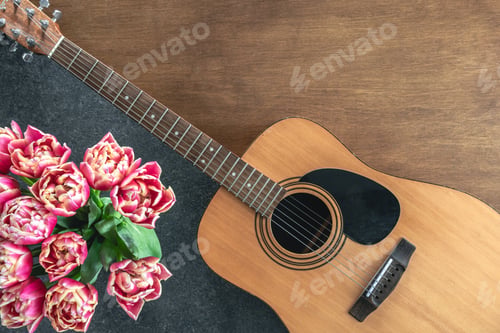 Preview: Bouquet of pink tulips and acoustic guitar on a wooden background, top view.