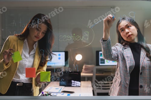 Preview: Businesswomen planning project strategy on glass board