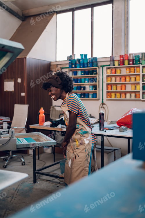 Preview: Smiling diverse graphic engineer preparing for silk screen printing.