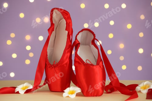 Preview: Pair of elegant pointe shoes and flowers on beige table against blurred lights, closeup