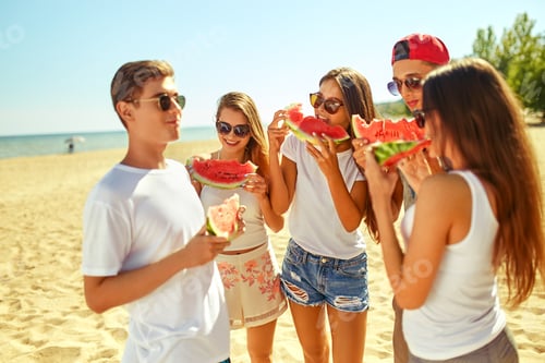 Preview: Group of friends having fun eating watermelon on beach. Excellent sunny weather. Super mood. Summer