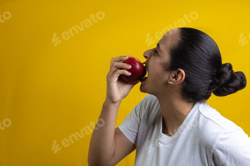 Preview: Hispanic woman biting red apple, on yellow background