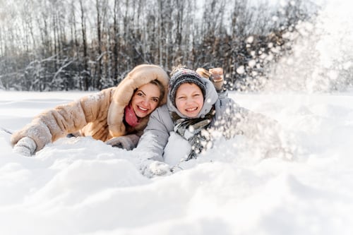 Vorschau: Ruhende Mutter mit jugendlichem Sohn auf weichem Schnee, nahe Gesichter, lächelnd nach den Winterspielen. Herzliche Familie