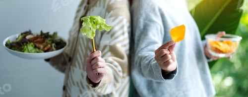 Preview: Two women holding and showing vegetables salad and potato chips for healthcare concept