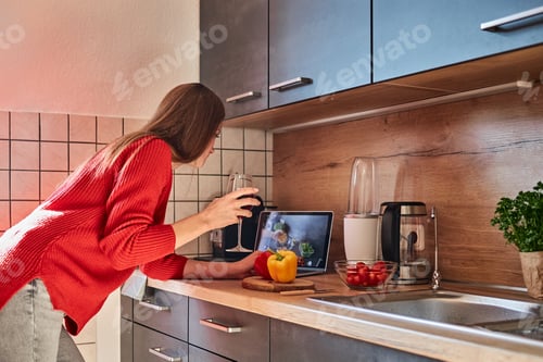 Preview: A young woman prepares a salad in the kitchen online and drinks red wine. Cooking courses online