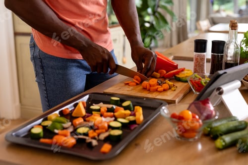 Preview: Midsection of african american man chopping vegetables using tablet in kitchen